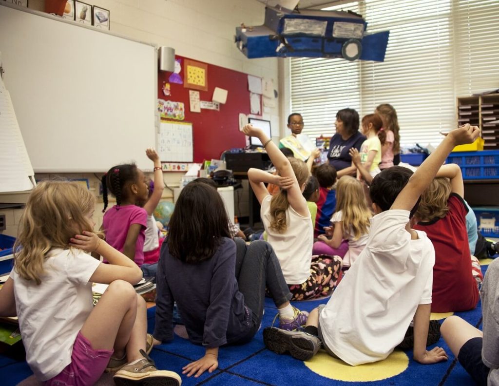 Audience of school children seated on floor before teacher reading storybook