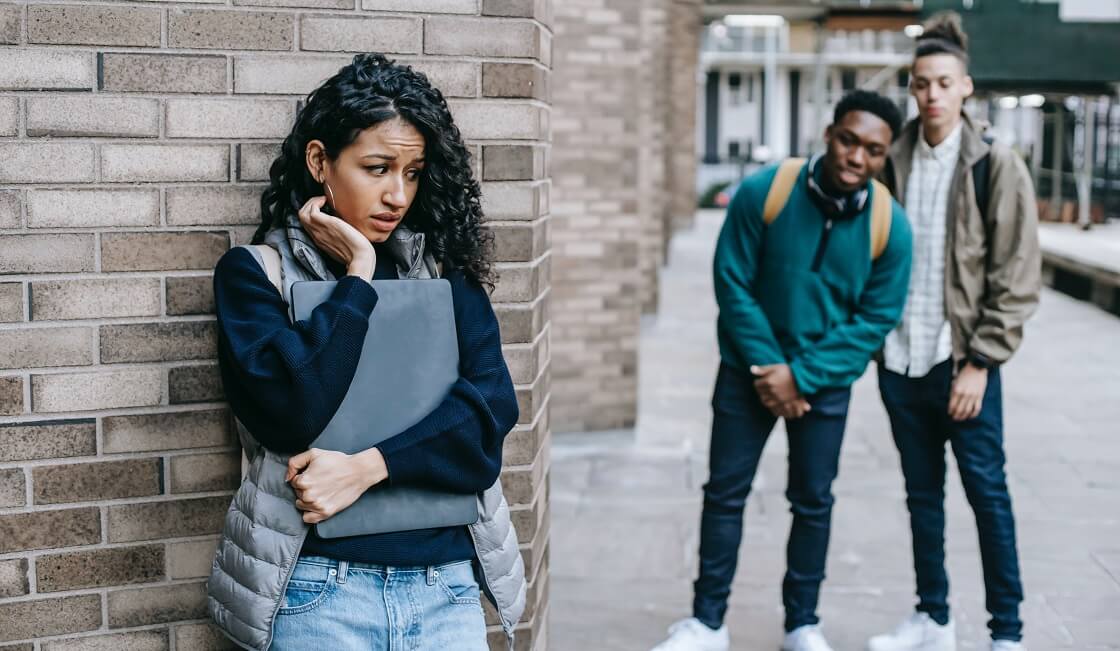 Female student hiding from bullies behind brick