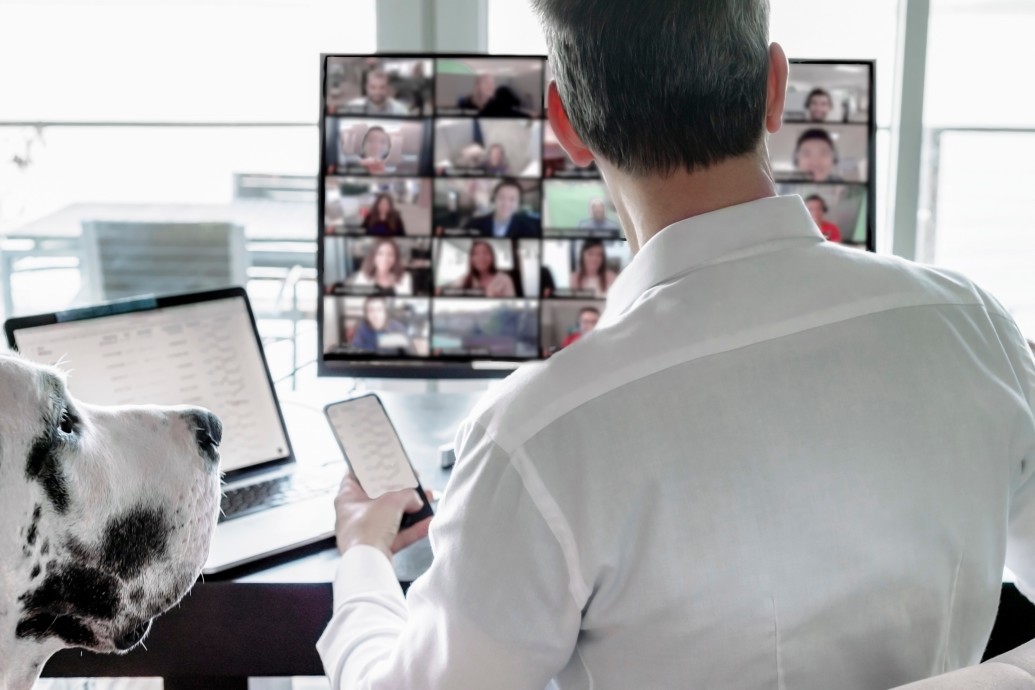 white male sitting at work desk with a dog and a conference call on screen