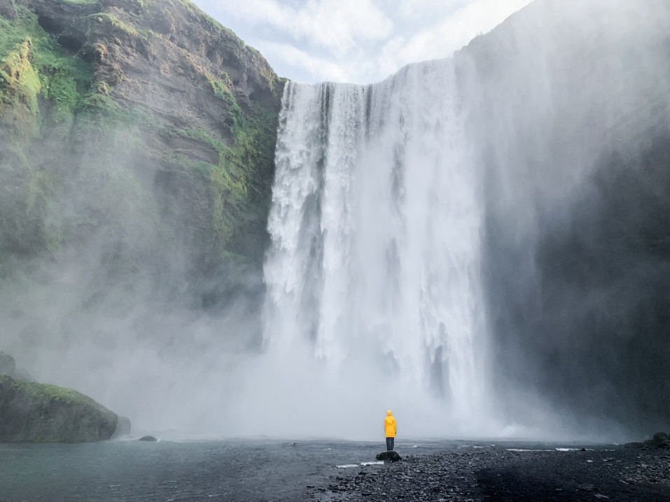 Person in yellow jacket standing near a large waterfall