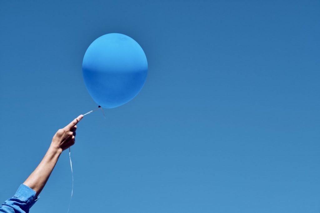 Person holding a blue balloon against the blue sky