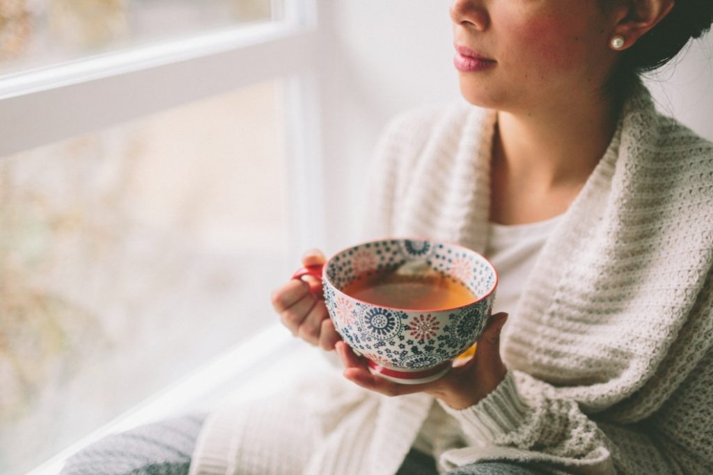 Woman drinking tea near window at home