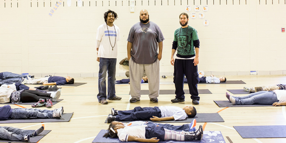 Teachers standing with kids laying down on mats in school gymnasium