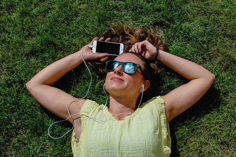 Woman smiling, laying on grass with earphones in