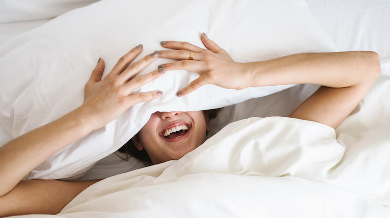 Woman in bed with pillow over eyes laughing