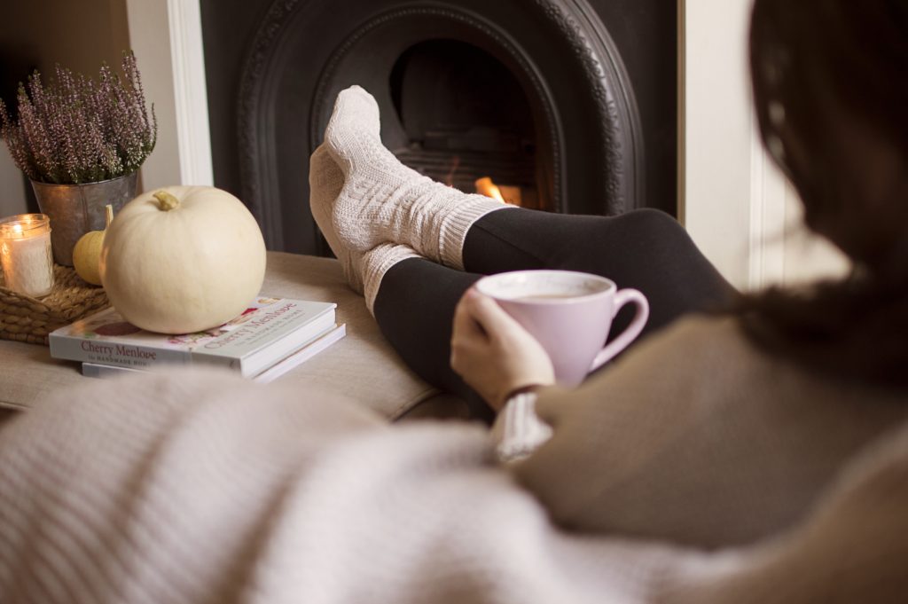 a woman sits with her feet up next to a fire the atmosphere is cosy and the socks are wooly t20 a82ZGv
