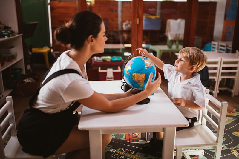 Teacher sitting with boy looking at a globe