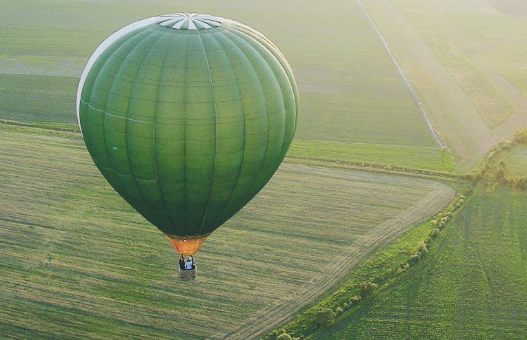 Green hot air balloon over green fields at sunset