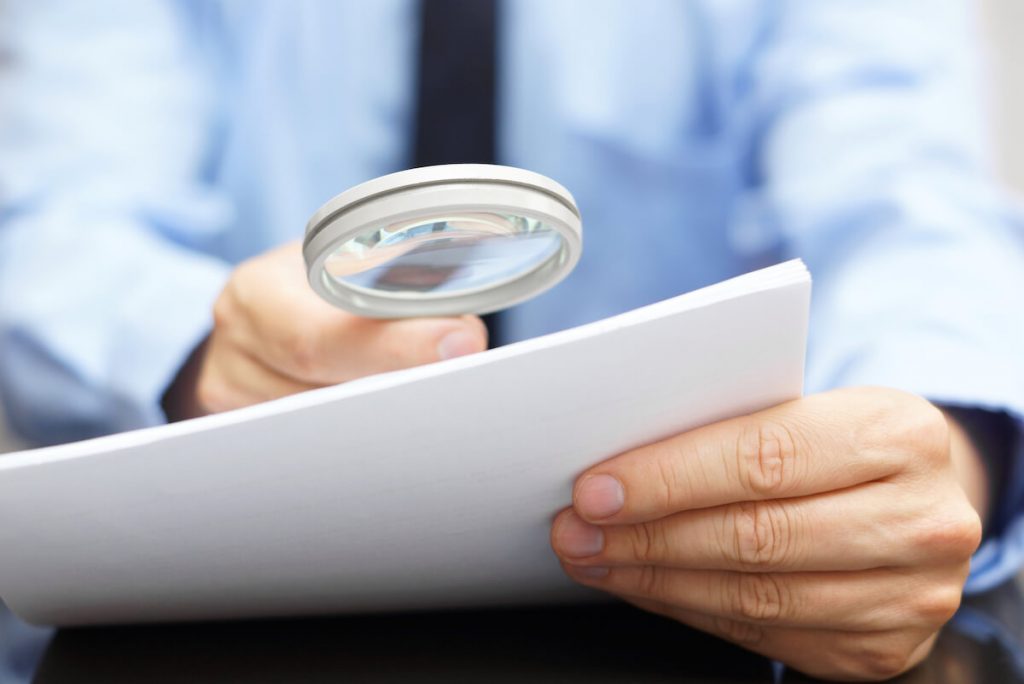 male businessman looking at papers with magnifying glass