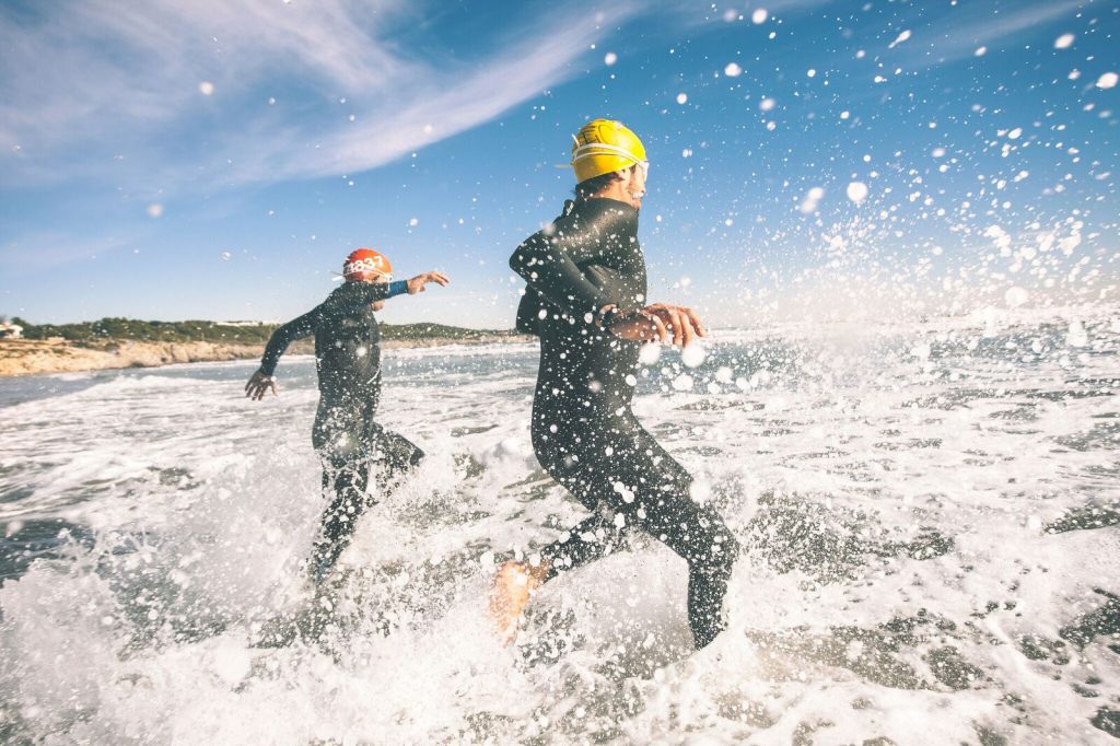 people running in the ocean in wet suits