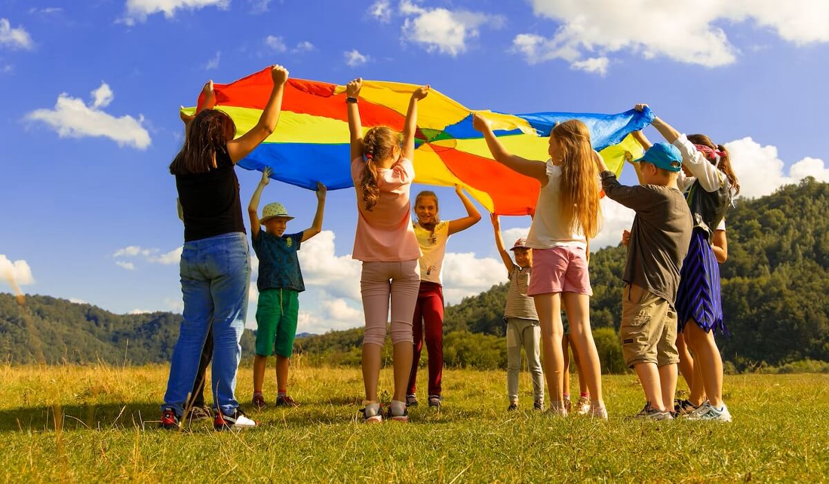 group of students holding rainbow tarp in green grass field during daytime