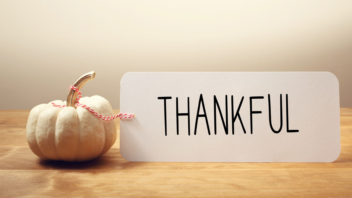 Thankful written on notecard next to miniature white pumpkin