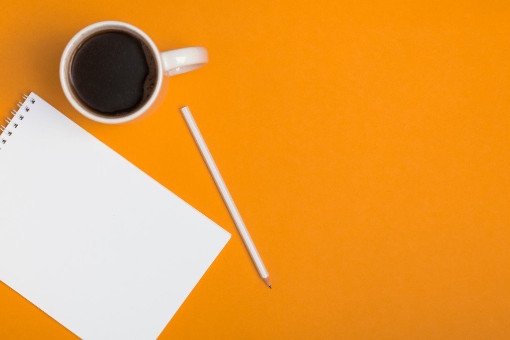 Pencil, note book and coffee on orange table