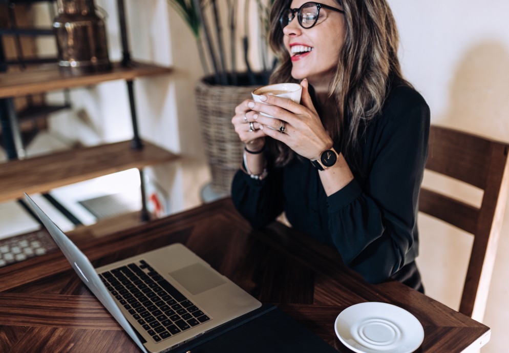 Woman drinking coffee and using laptop at her desk