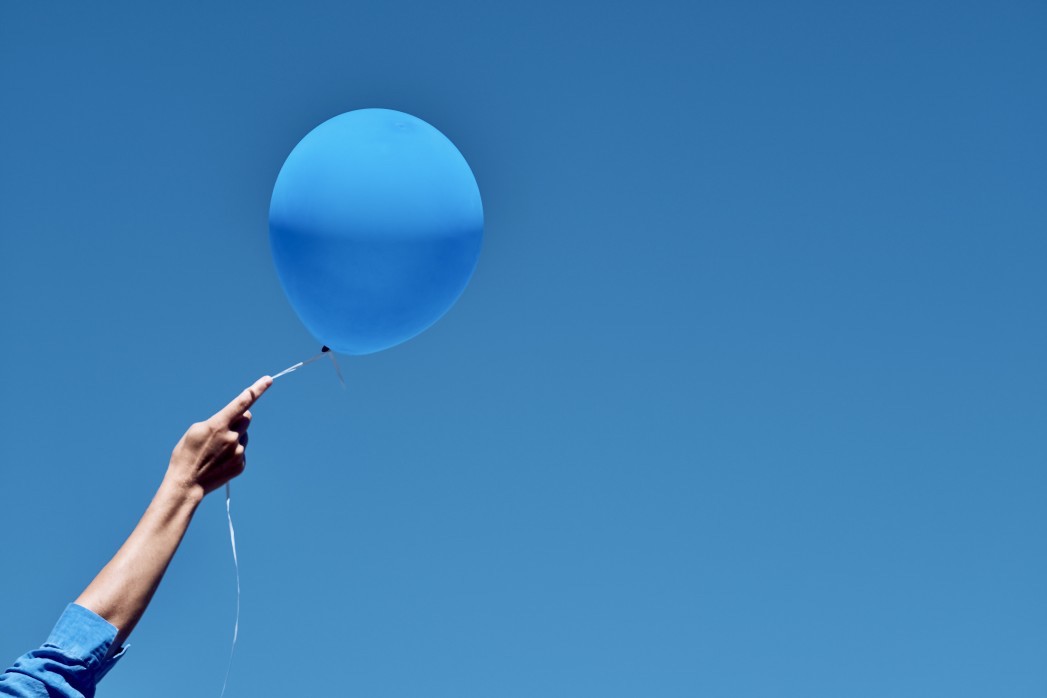 Person holding a blue balloon against the blue sky