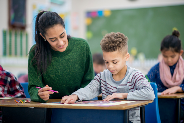 Woman teacher aids student with coloring sheet