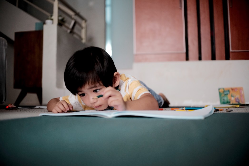 Young boy laying on floor drawing