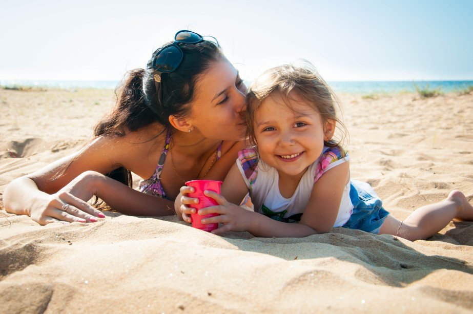 Mom kissing daughter while laying on sand at the beach