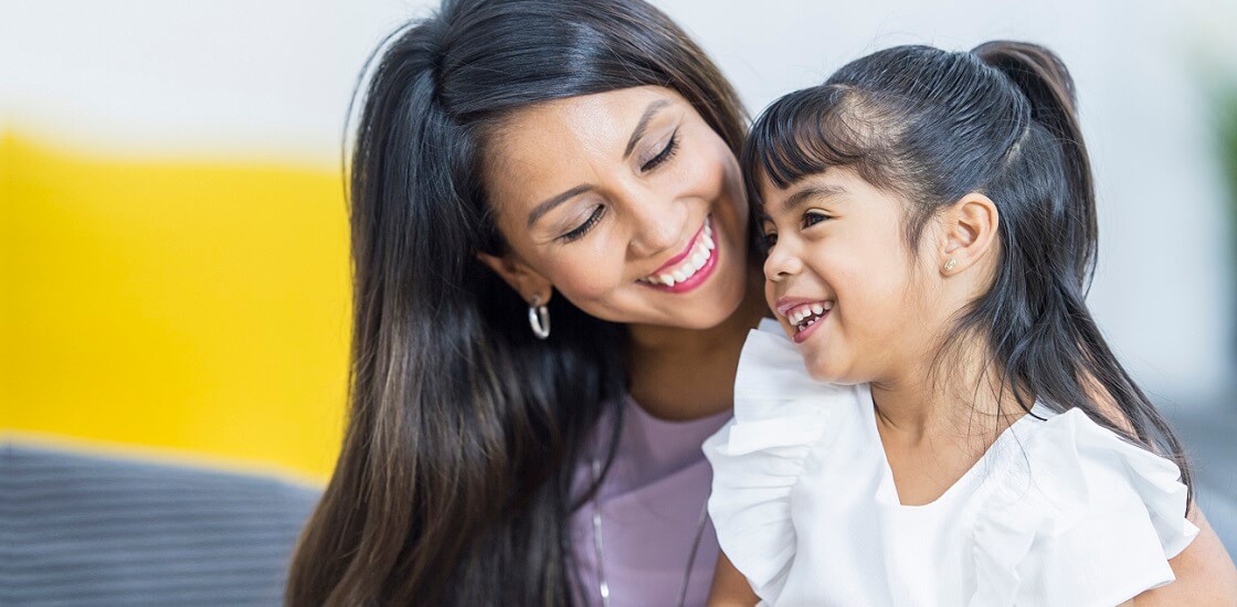 Ethnic mother and daughter on couch together with the daughter in mother's lap