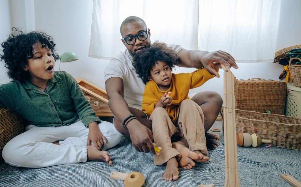 African American father playing with kids on floor with wood train set