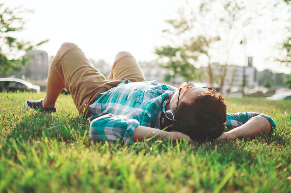 Boy laying on back in grass field using headphones