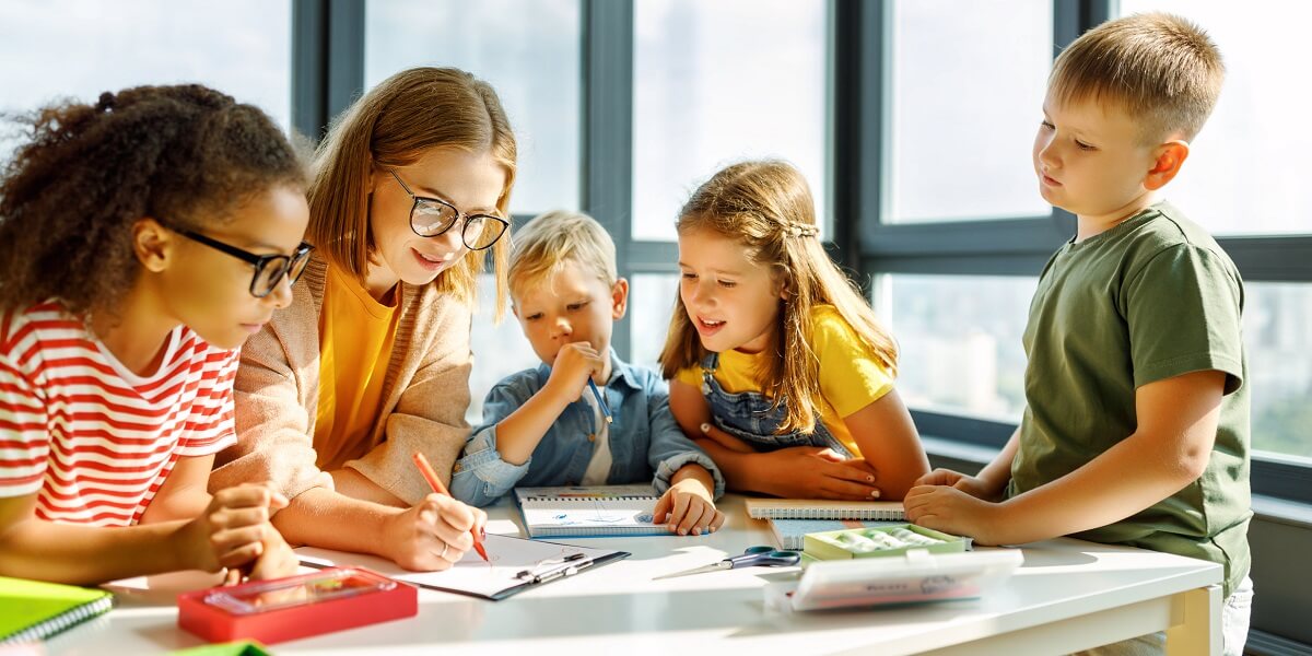 Happy female tutor and students around table at school smiling
