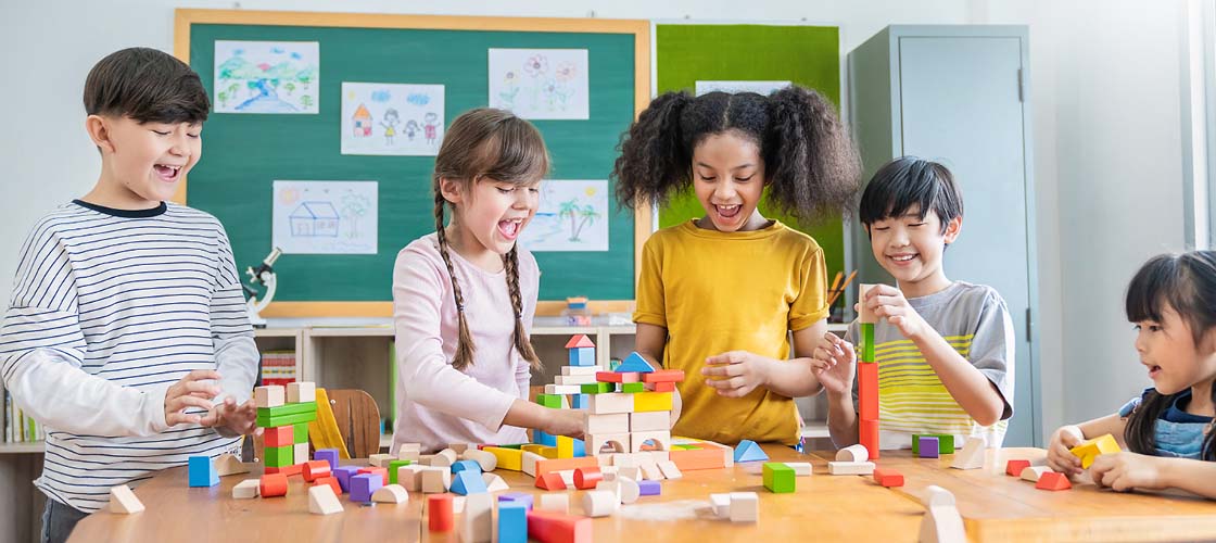 Diverse group of students laughing playing with colorful wooden blocks