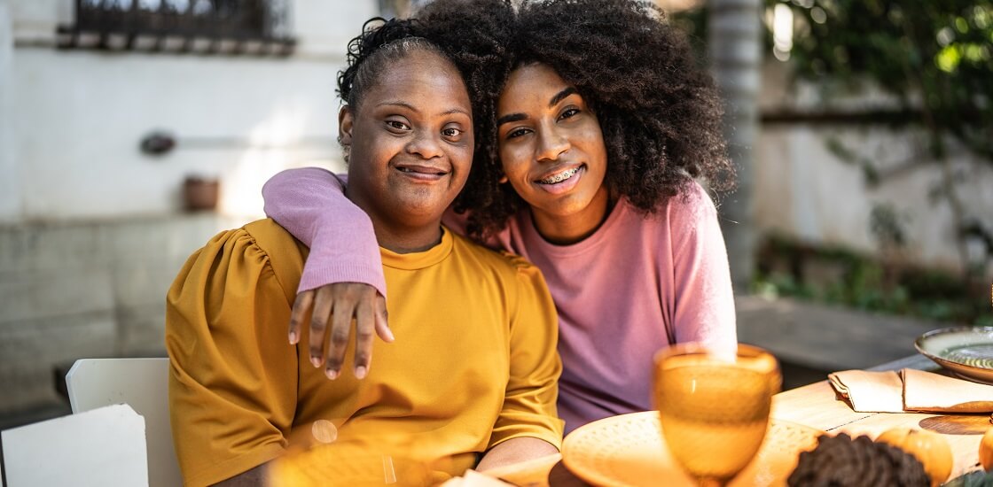 Portrait of sisters embracing during lunch at home including special needs woman