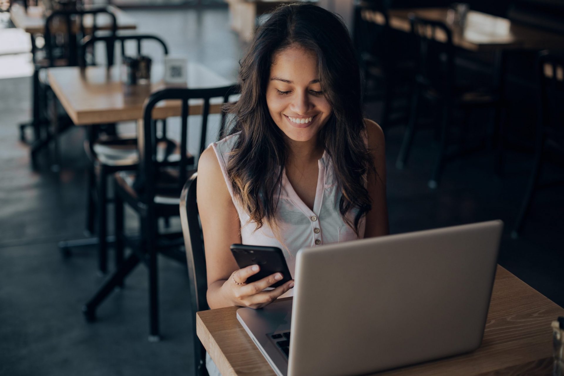 young woman smiling at phone in coffee shop t20 koLELE scaled