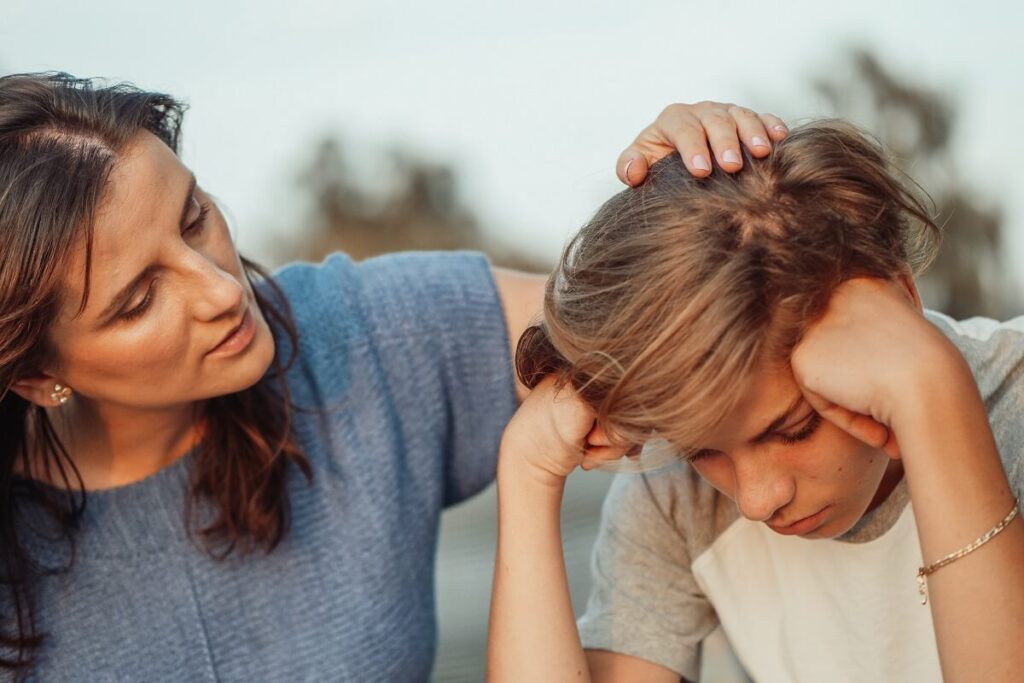 Mom in blue shirt comforting stressed out teenage son in white shirt