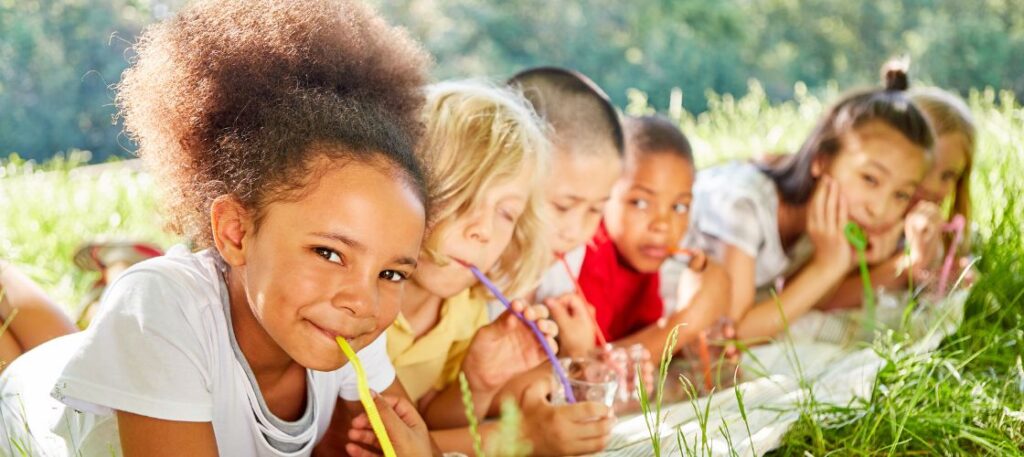 Children laying in field drinking from cups with colorful straws