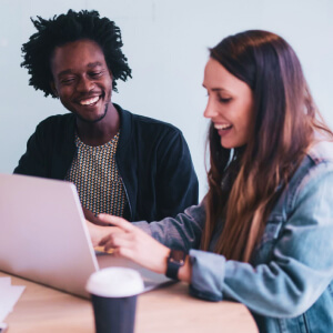 African American male and Caucasian woman working on laptop drinking coffee