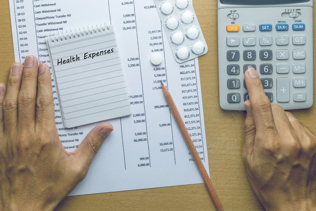 Man calculating health expenses with medication, calculator and notes on a table