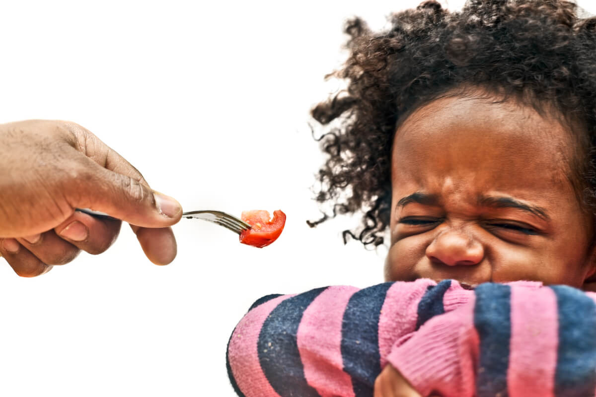 close up of African American toddler girl refusing to eat tomato