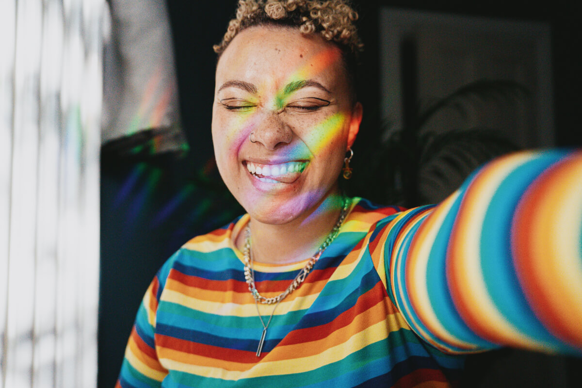 Portrait of nonbinary neurodiverse person wearing a rainbow sweater smiling taking selfie
