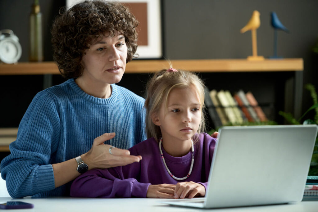 Mother explaining online safety to her daughter on laptop while sitting at desk