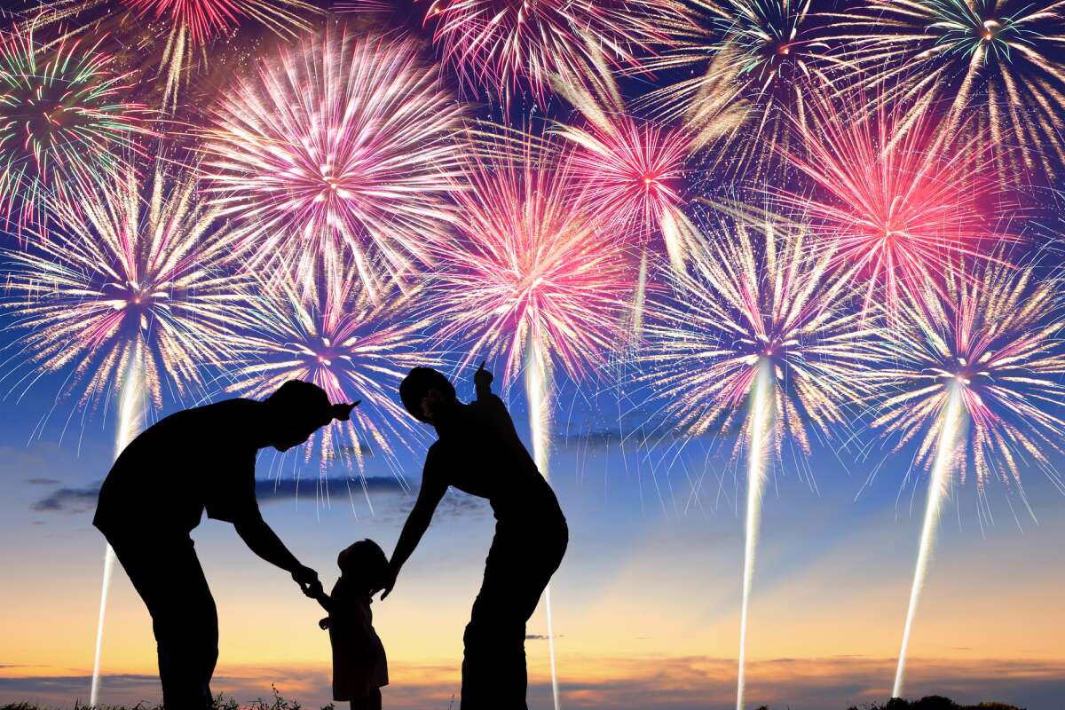 Silhouette of mother and father showing young child fireworks in night sky