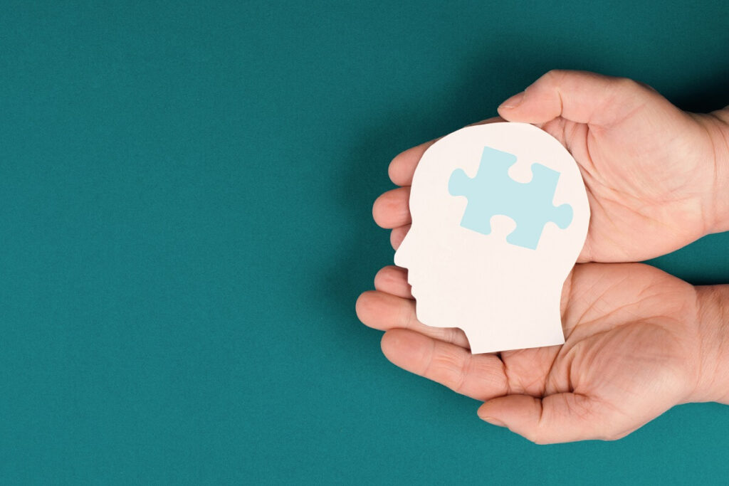 Hands cupped together holding a head with puzzle piece representing Autism