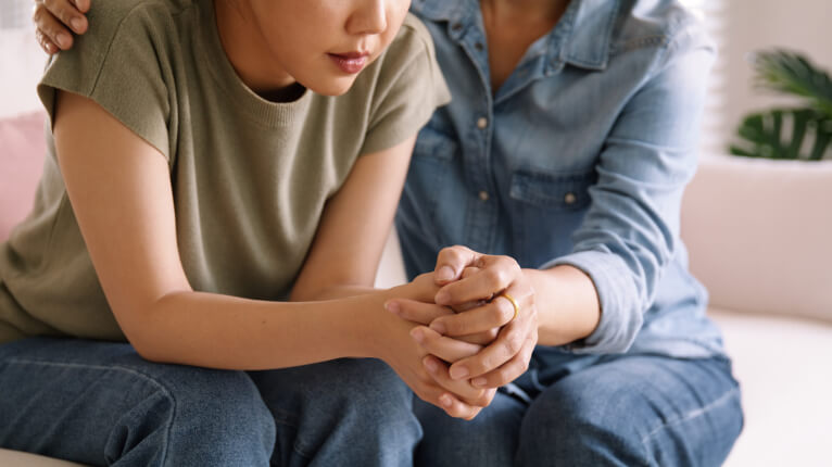 Mom comforting young stressed daughter by holding her hands and shoulder