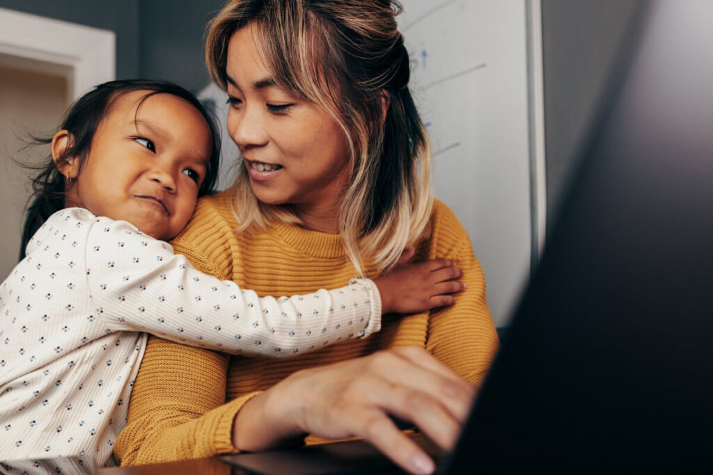 Working mom in home office trying to find work/life balance while daughter embraces her for attention