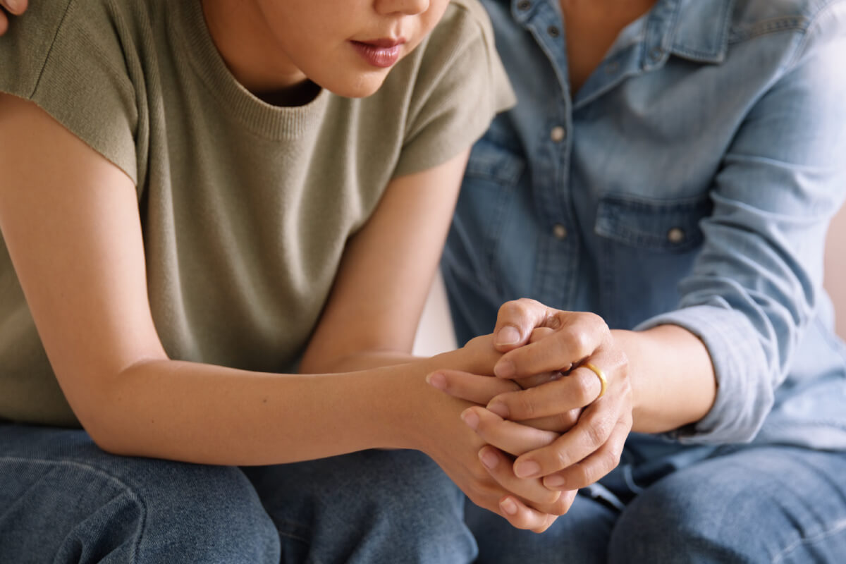 mom holding stressed daughter's hand and shoulder on couch