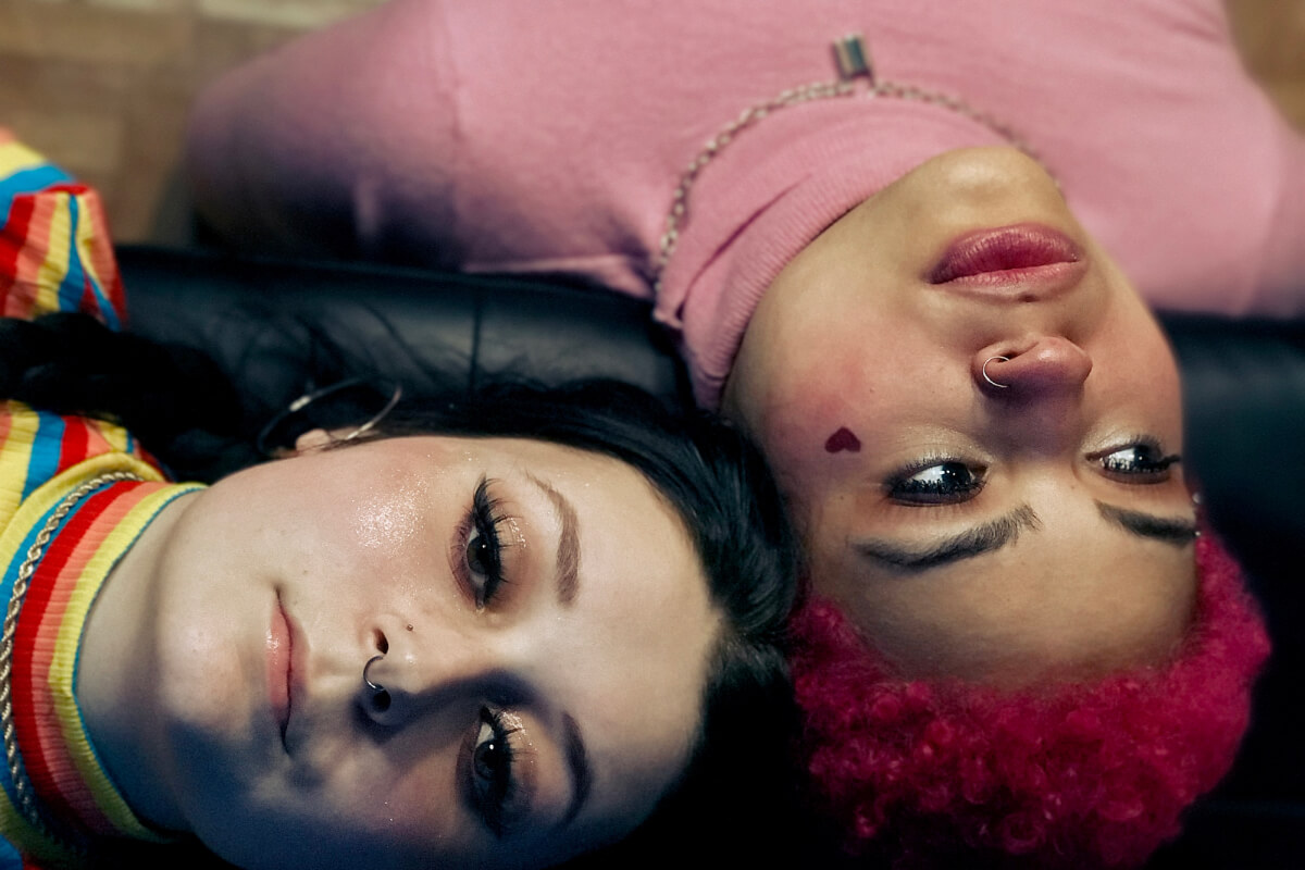 Two autistic, gender neutral teens on sofa wearing colorful clothing