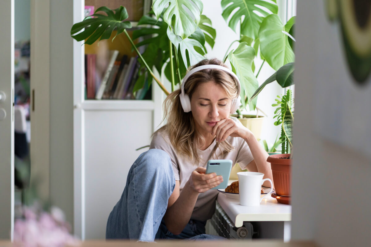 Woman by window listening to behavioral health podcast on smartphone