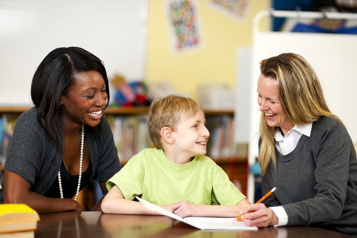 Two female teachers assisting young male student with cerebral palsy in special education classroom