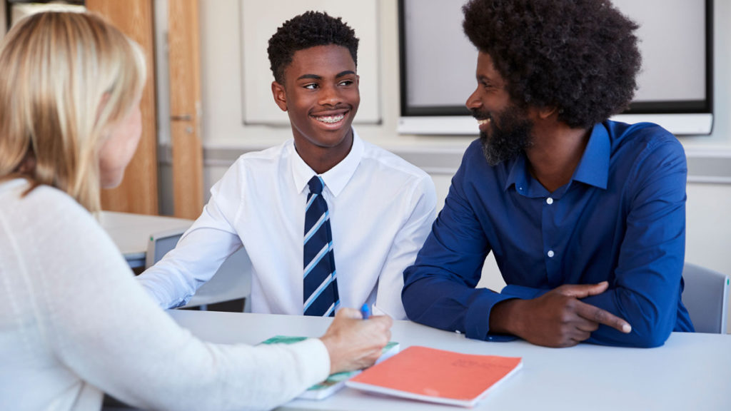 African American father and son talking with female Caucasian teacher