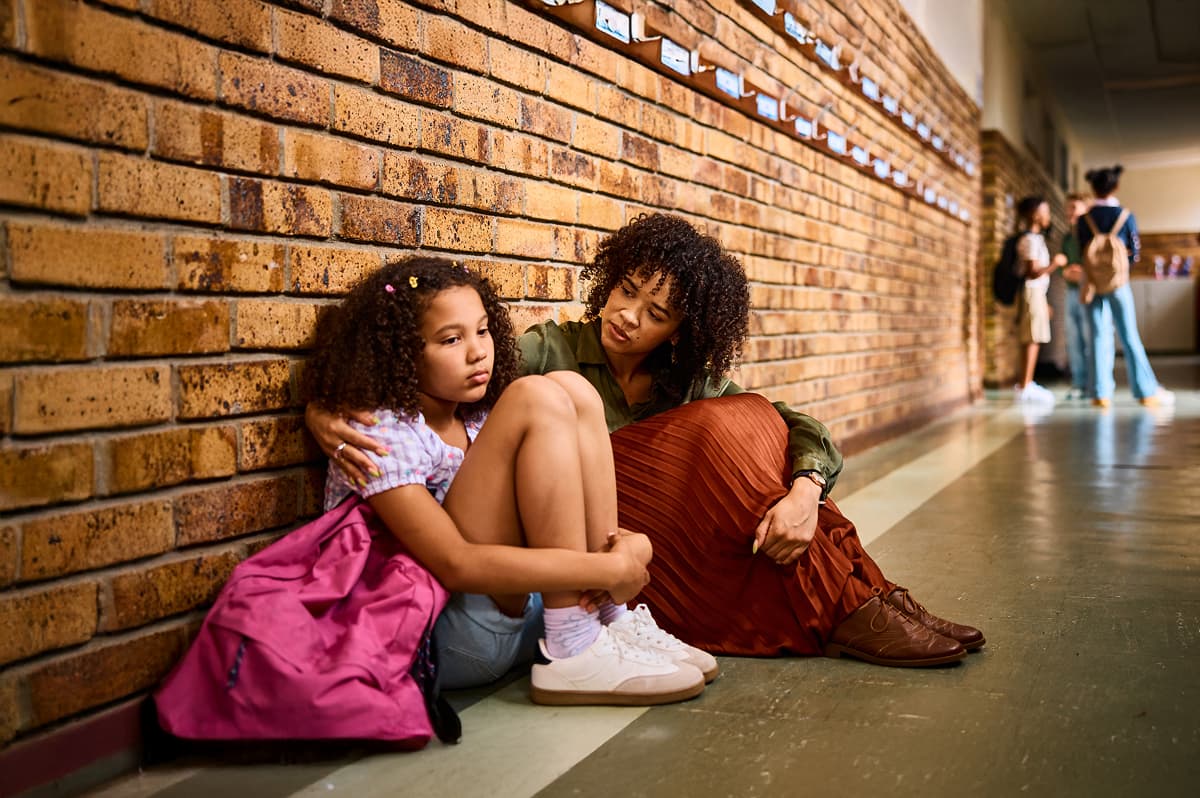 School teacher on hallway floor against wall beside upset schoolgirl