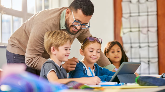 Elementary students working on digital tablets with help of teacher