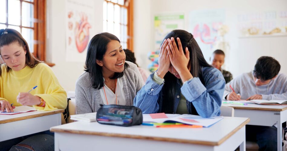 Female teacher helping frustrated girl student at her classroom desk