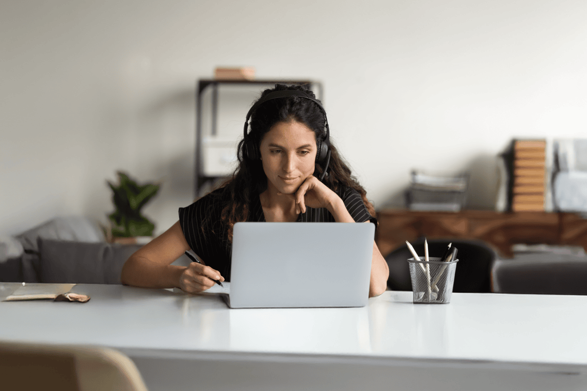 Woman with headset taking notes at a laptop.