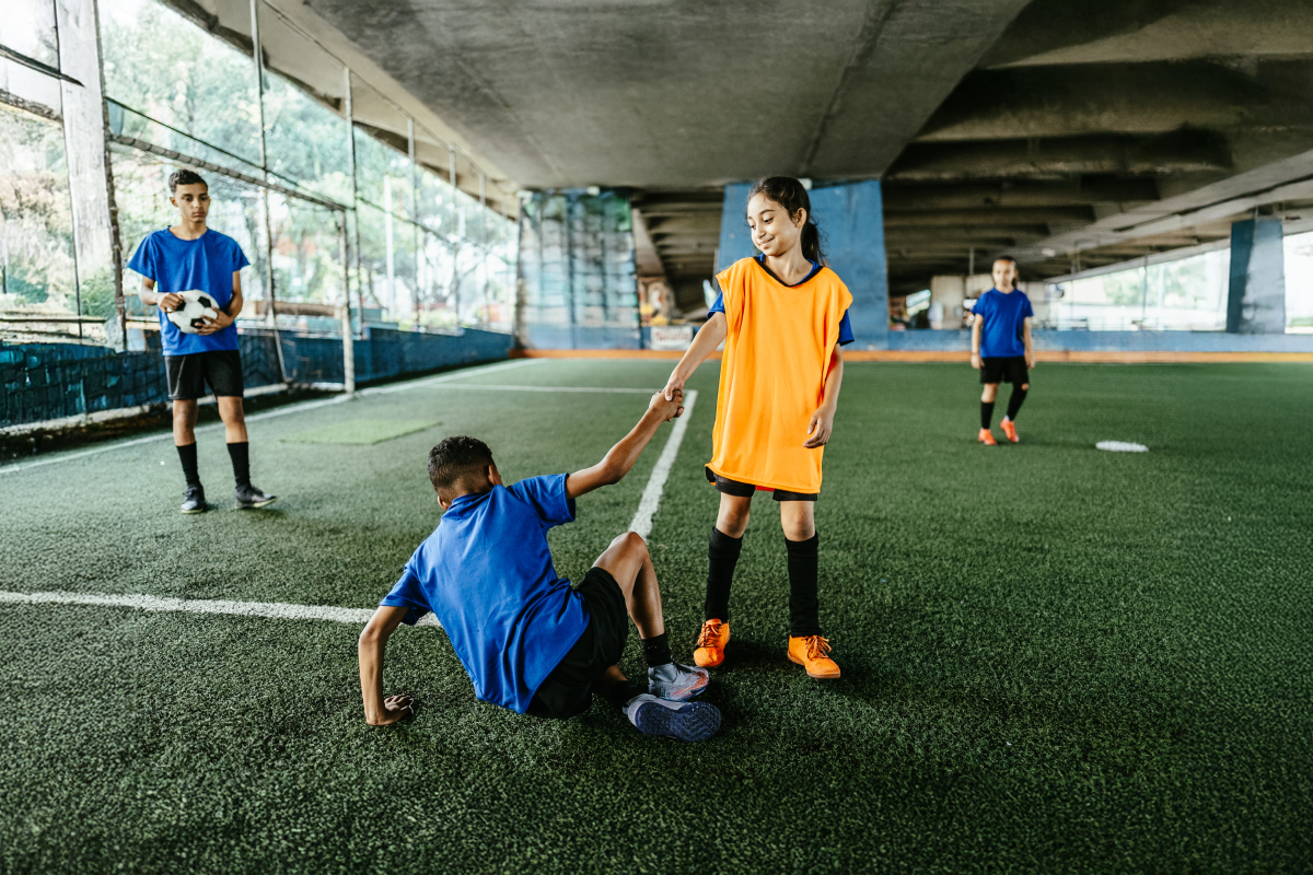 Soccer player helping opponent up, showing sportsmanship.